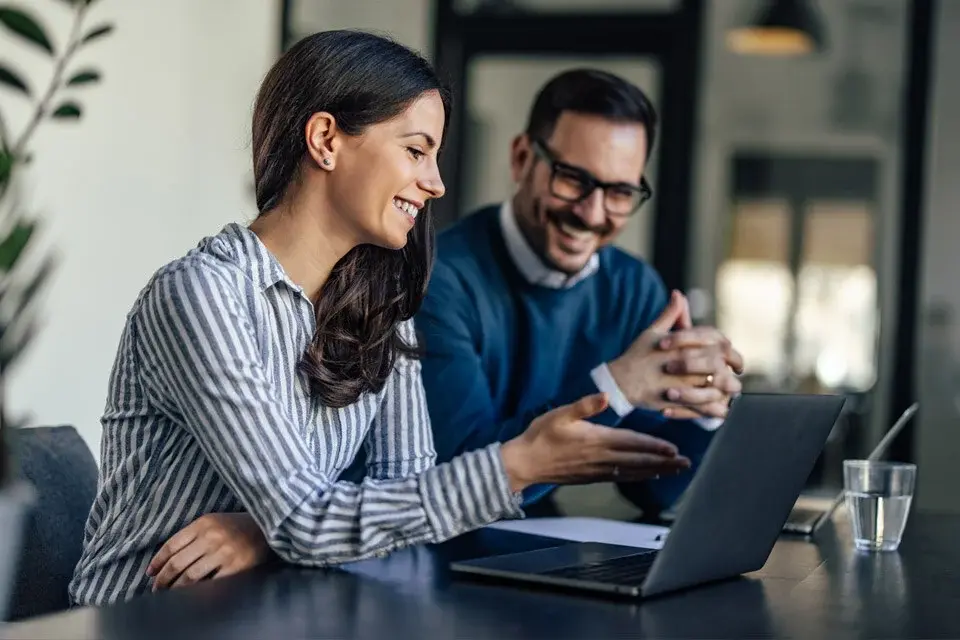 Professional woman explaining something on a laptop screen to a male colleague.