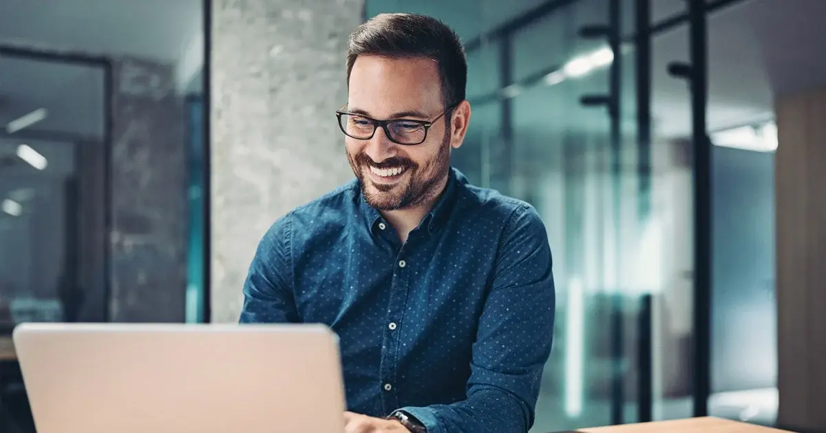 Professional man with glasses smiling while working on laptop.