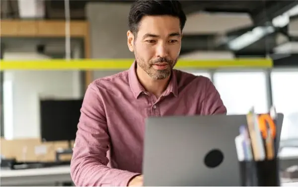 Man in red shirt working on laptop in office.