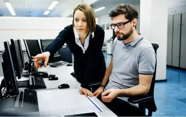 Female manager pointing out issue on computer screen to male office employee.